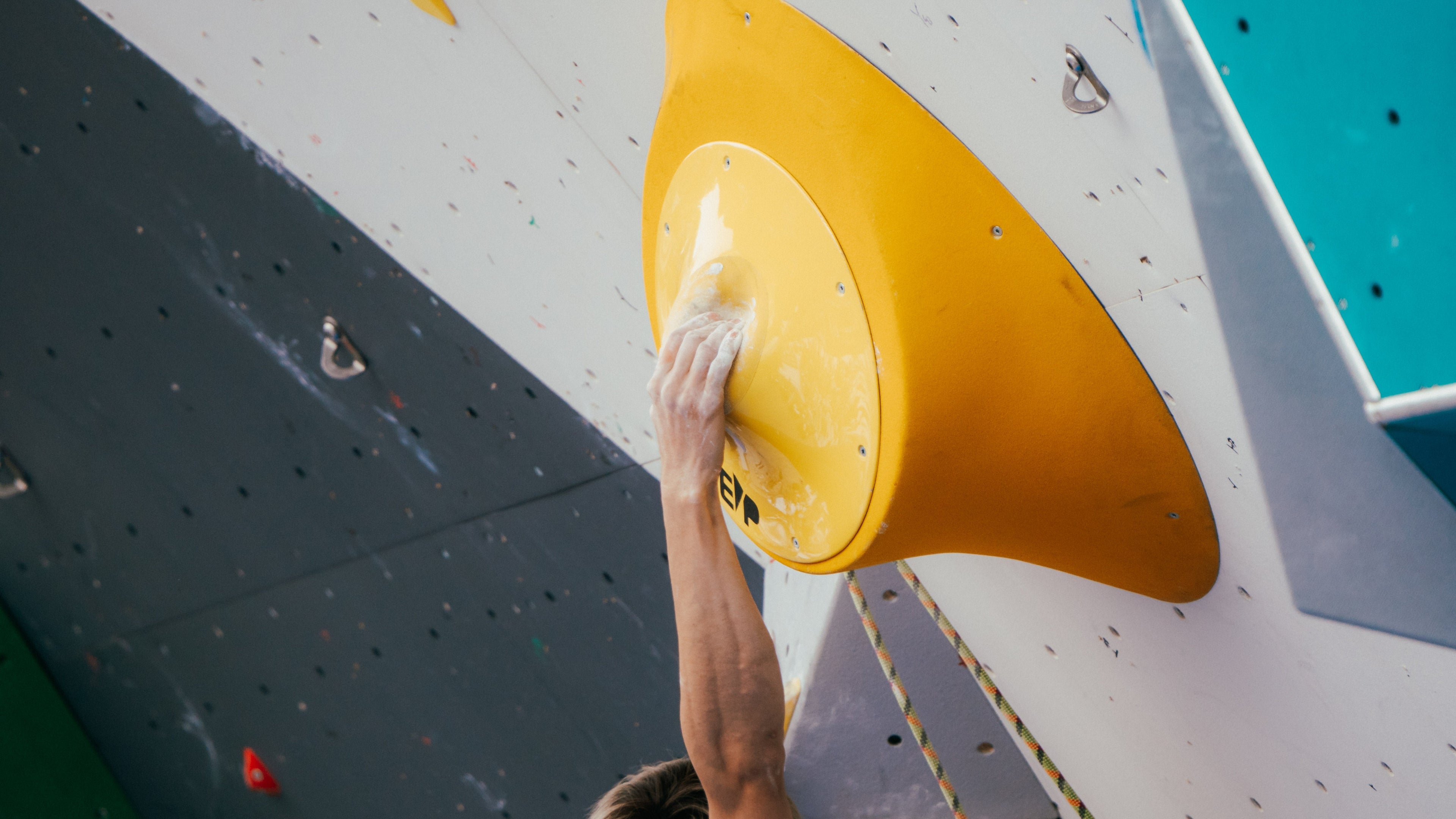 Person climbing a wall with a yellow holds, focusing on hand placement.